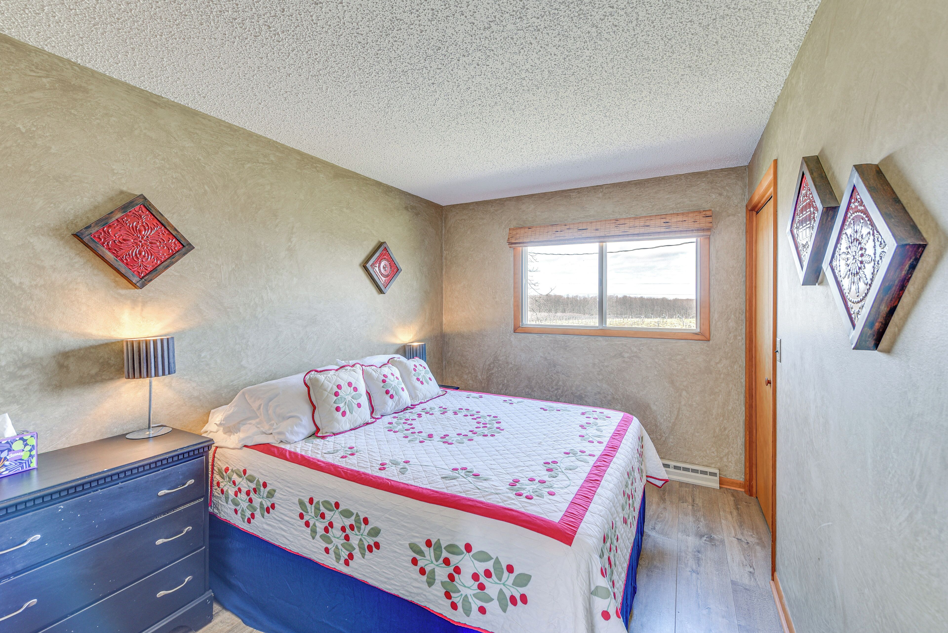 A bedroom with a bed, a dresser, a window, and decorative wall art.