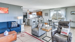 Un salon avec un canapé, un fauteuil et une table basse, une cuisine à l’arrière-plan et une vue par la fenêtre.