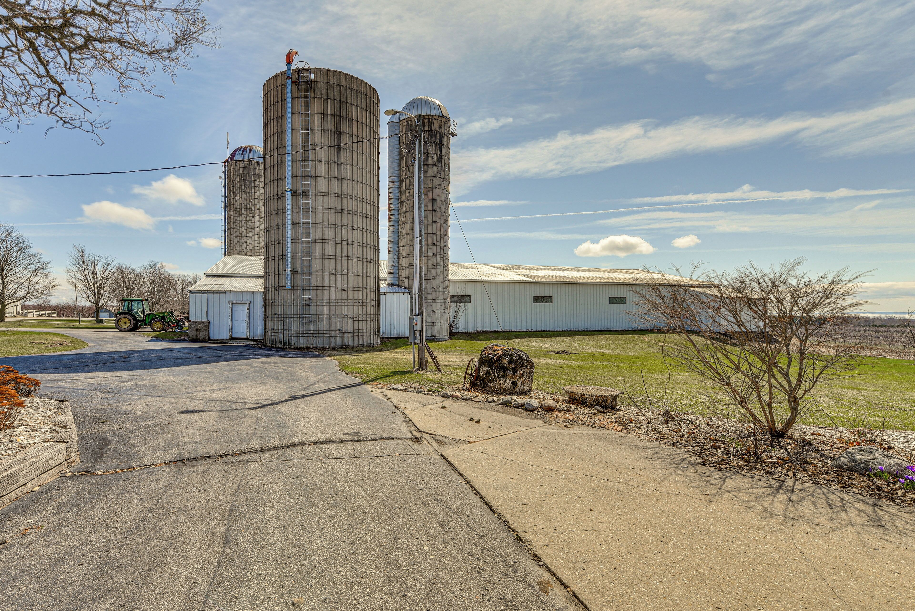En stor industribygning med to høje silos, en asfalteret indkørsel og en traktor i baggrunden.
