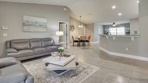 A modern living room with a gray sofa, a coffee table, and a dining area with chairs and a table. - Central Florida Retreat Near The Villages & Golf! (Summerfield)