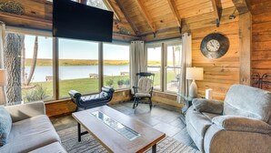 Una sala de estar acogedora con un ventanal grande, un televisor de pantalla plana, techo de madera y vistas al exterior.