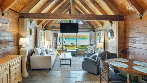 Interior de una cabaña de madera con televisión, zona de estar y vista al océano.