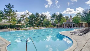 Una piscina con sedie a sdraio, un'area salotto coperta e un edificio con un camino sullo sfondo.