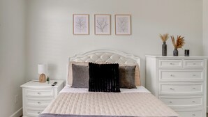Una camera da letto ordinata con un letto, comodini, una cassettiera e stampe botaniche incorniciate alle pareti.