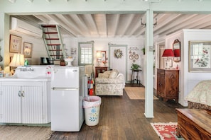 A kitchen with a refrigerator, stove, and sink; a wooden ladder; a floral-patterned sofa; a wooden cabinet; and a red lamp.