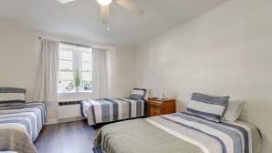 A bedroom with two beds, a window with curtains, a ceiling fan, and a nightstand.
