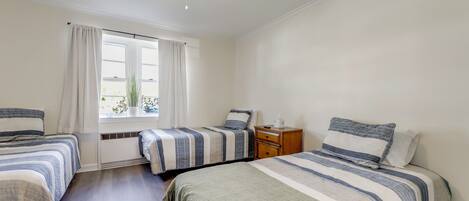 A bedroom with two beds, a window with curtains, a ceiling fan, and a nightstand.