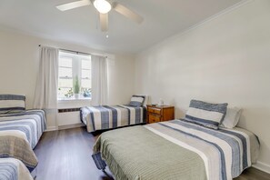 Un dormitorio con dos camas, una ventana con cortinas, un ventilador de techo y una mesita de noche.
