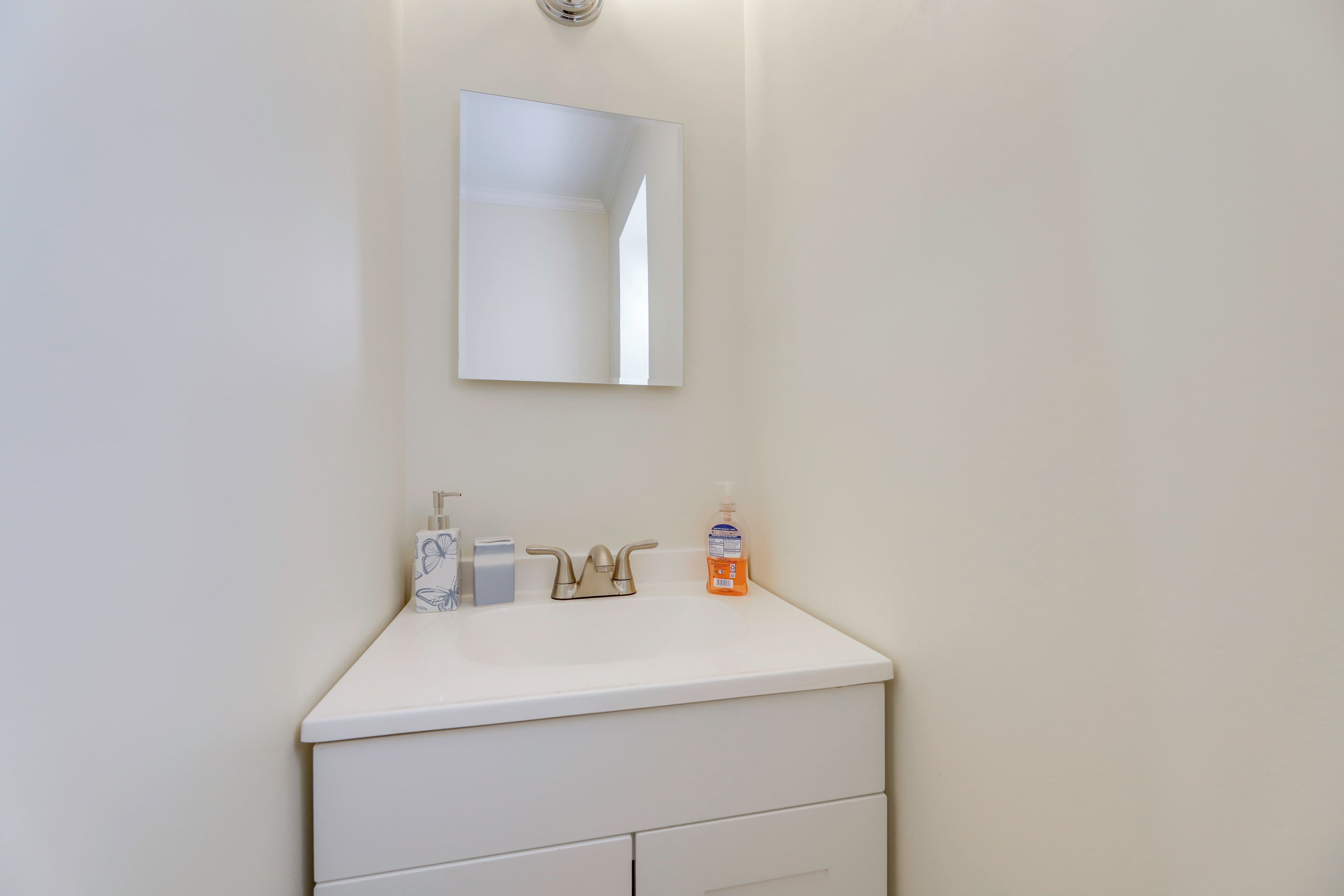 A bathroom with a white sink, a mirror, a faucet, and a soap dispenser.