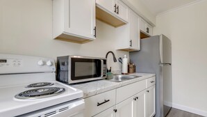 A kitchen with white cabinets, a microwave, a stove, a sink, and a refrigerator.