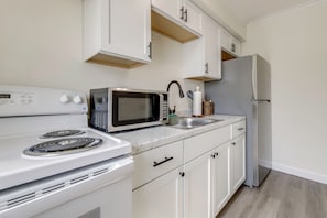 Una cocina con armarios blancos, microondas, estufa, lavaplatos y refrigerador.