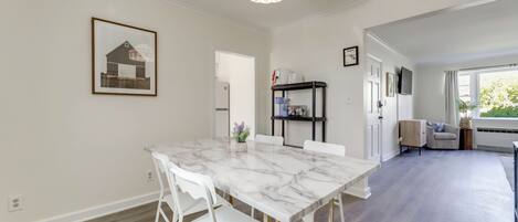 A dining area with a marble table, white chairs, a chandelier, and a framed picture on the wall.