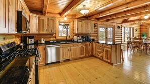 A spacious log cabin kitchen with wooden cabinets, a stainless steel stove, and a dining area with a table and chairs. - Group Fun on Tittabawassee River! Large Log Cabin (Beaverton)