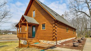 A log cabin with a porch, a chimney, and a stone foundation. - Group Fun on Tittabawassee River! Large Log Cabin (Beaverton)