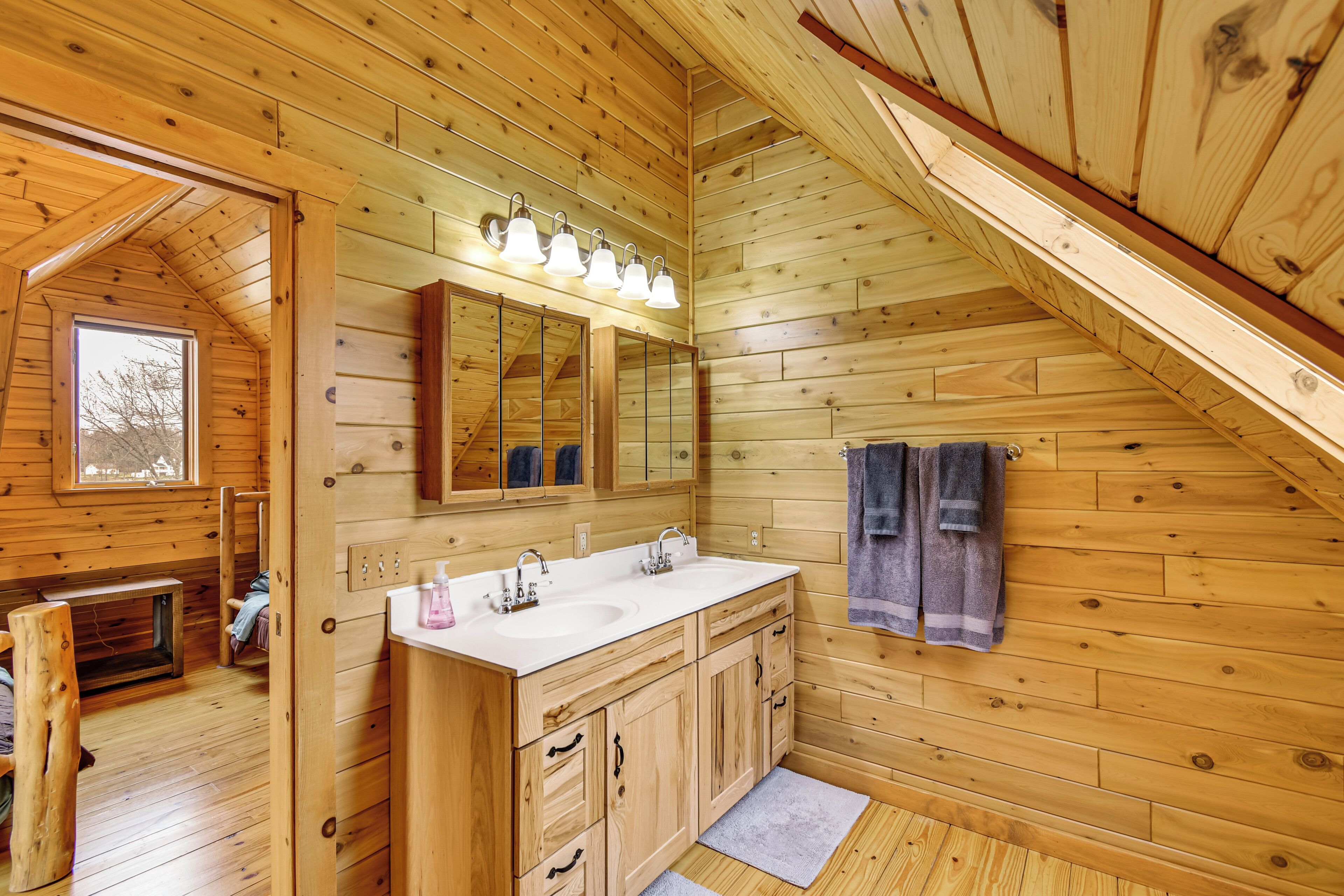 Une salle de bain rustique, avec des murs en bois, un grand miroir, deux lavabos et une serviette accrochée au mur.