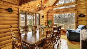 A log cabin interior with a dining table, chairs, a chandelier, and a sofa. - Group Fun on Tittabawassee River! Large Log Cabin (Beaverton)
