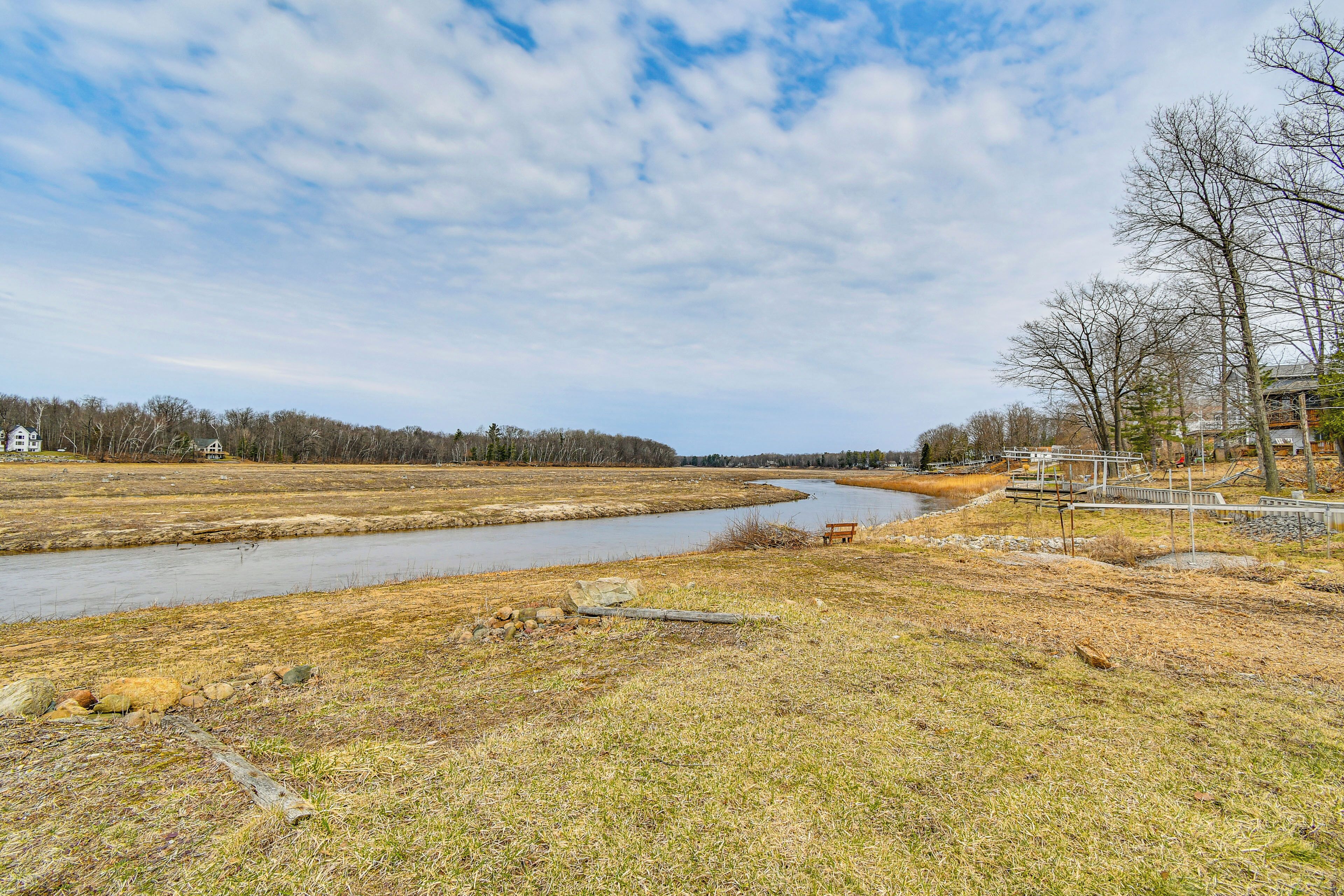 A river flowing through a grassy area with a bench and a building in the background.