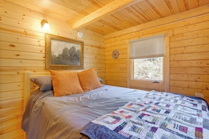 Habitación de cabaña de madera con cama, un reloj de pared, un cuadro enmarcado y una ventana con persianas.