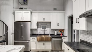 A modern kitchen with white cabinets, stainless steel appliances, and a marble countertop.