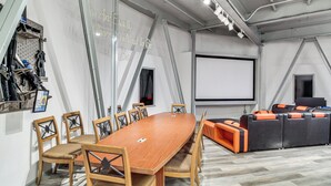 A conference room with a long table, chairs, a projector screen, and a seating area with cushions.