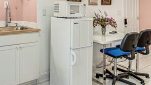 Een kitchenette met een magnetron, wastafel en kastjes; een kleine tafel met stoelen; en een deur met een code slot.