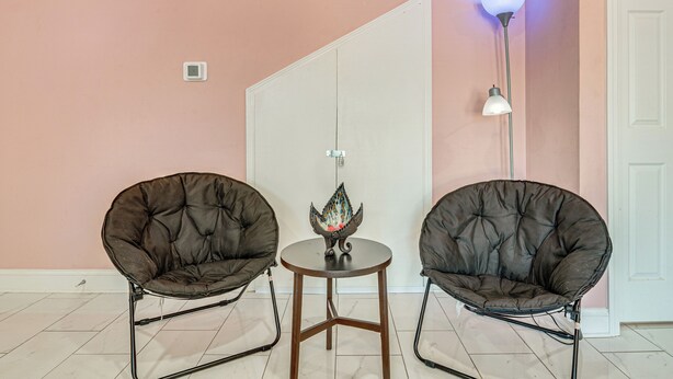 Twee comfortabele fauteuils, een bijzettafeltje met een decoratief object, een vloerlamp, en een witte deur in een kamer met roze wanden.