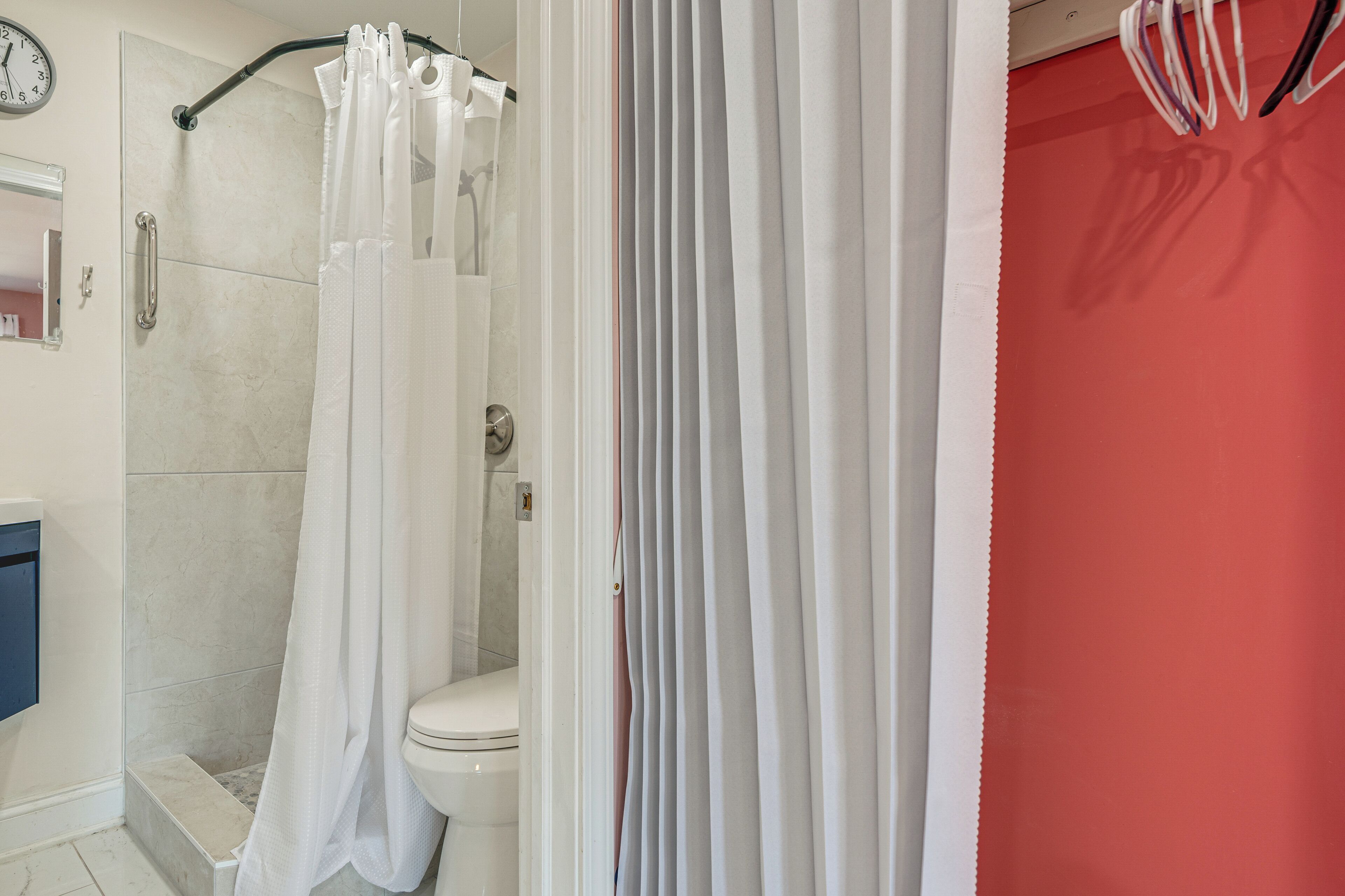Ein Badezimmer mit Dusche, Toilette und einer Uhr an der Wand.