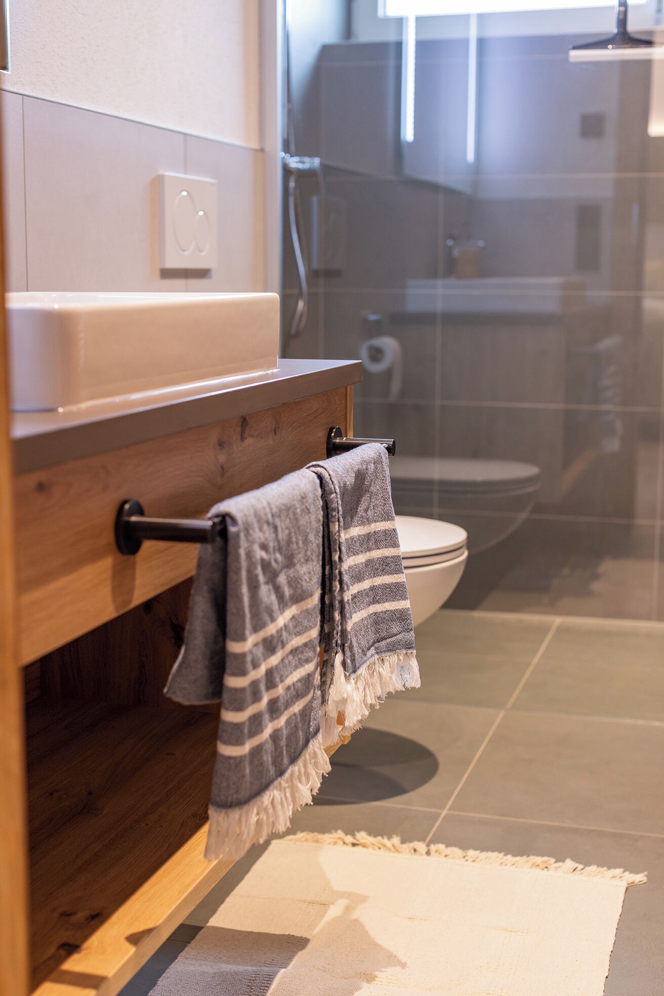 A bathroom with a wooden vanity, a towel hanging on a towel rack, a toilet, and a glass shower enclosure.