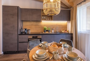 A modern kitchen with dark cabinetry, a wooden countertop, and a dining area set with plates, bowls, and cups. - Lennis Apartments by we rent (Zell am See)