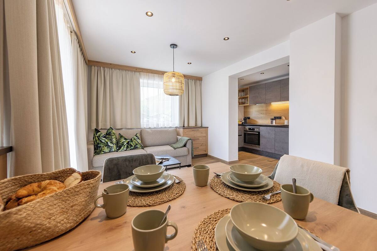 Una sala de estar moderna con un sofá, una mesa de comedor dispuesta con platos, tazas y una cesta de pan.