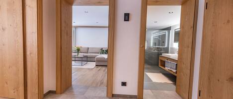 A hallway with wooden doors leading to a living room and bathroom.