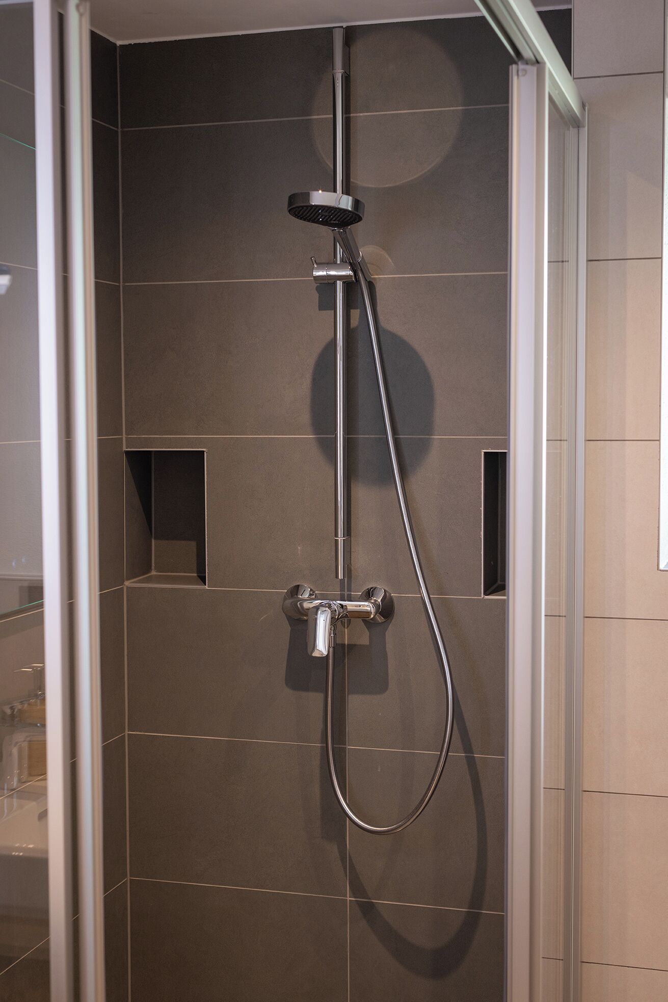 A shower with a handheld showerhead and a wall-mounted control.