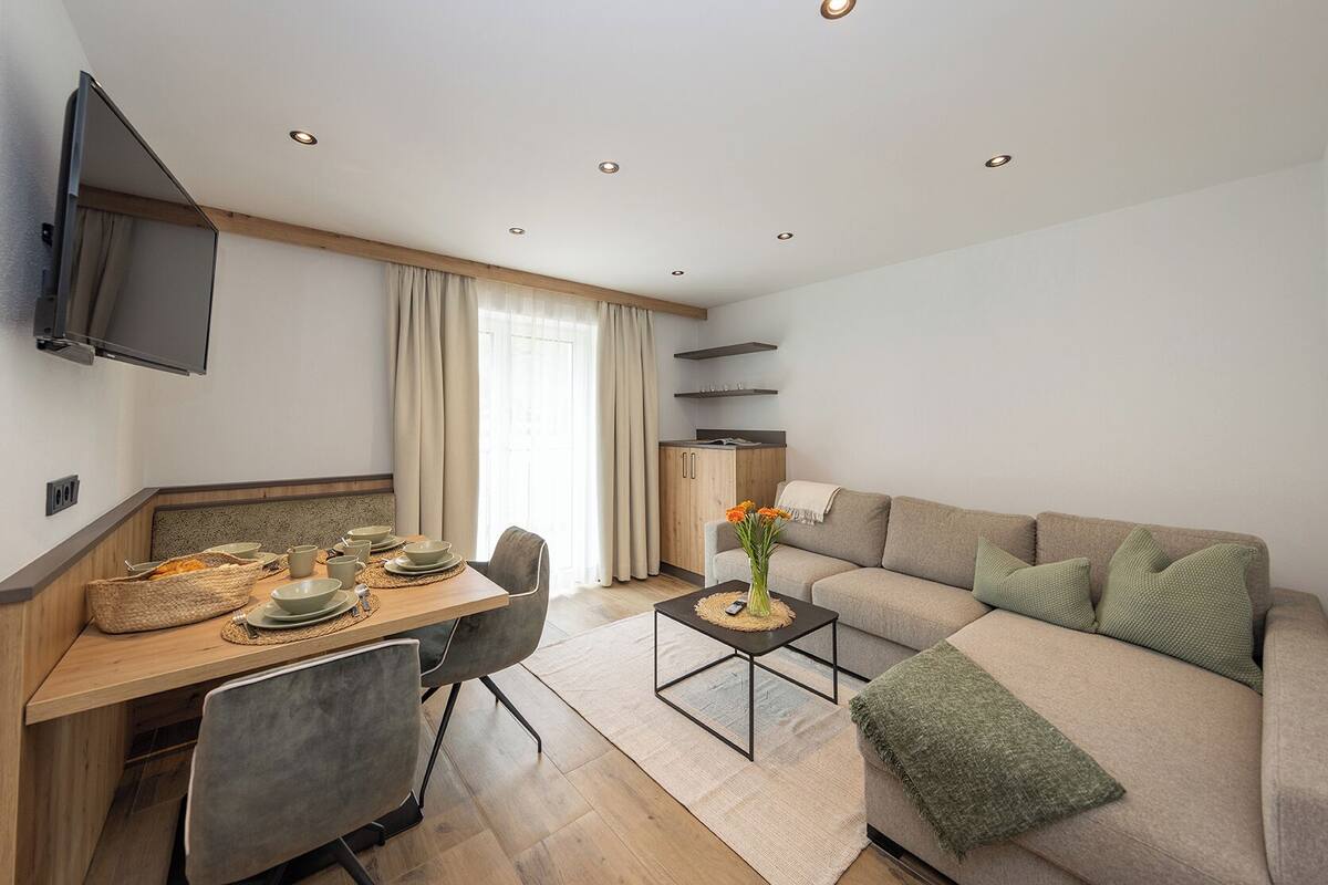 Un espacio de estar moderno con comedor, sofá, televisor y armarios de cocina.