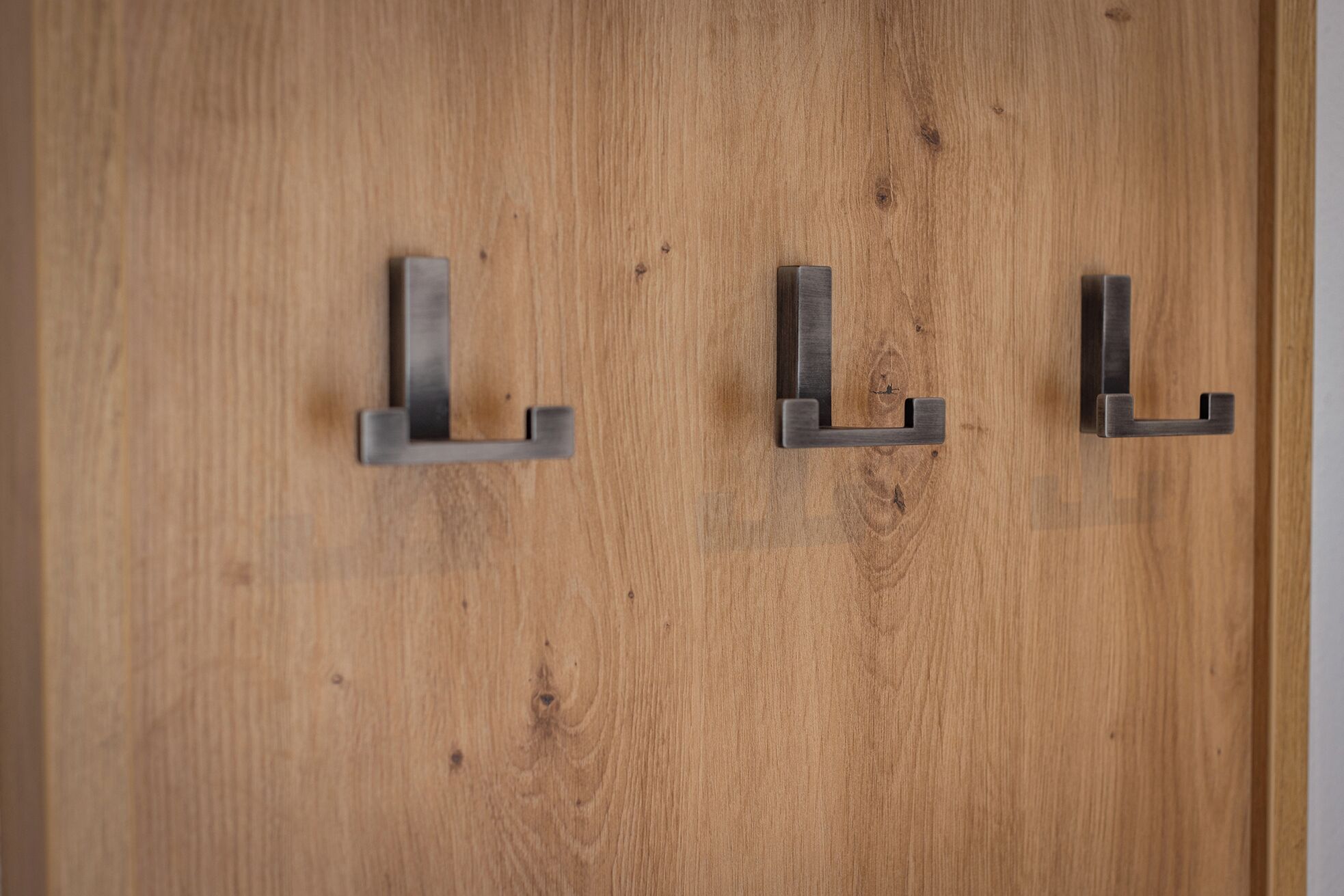A wooden door with three metal hooks.