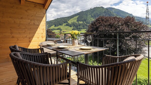 Un balcon avec une table dressée pour deux personnes, offrant une vue sur un paysage montagneux.