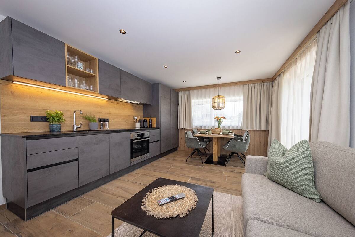 Una cocina moderna con electrodomésticos integrados, un comedor con mesa y sillas de madera, y una sala de estar con sofá y una mesa de centro.