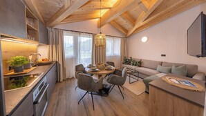 Une cuisine moderne avec des poutres en bois, un coin repas avec une table ronde et des chaises, un canapé et un téléviseur fixé au mur.