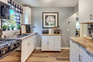 Une cuisine moderne avec des meubles blancs, une cuisinière à gaz, un coin café et un tableau représentant une fleur accroché au mur.