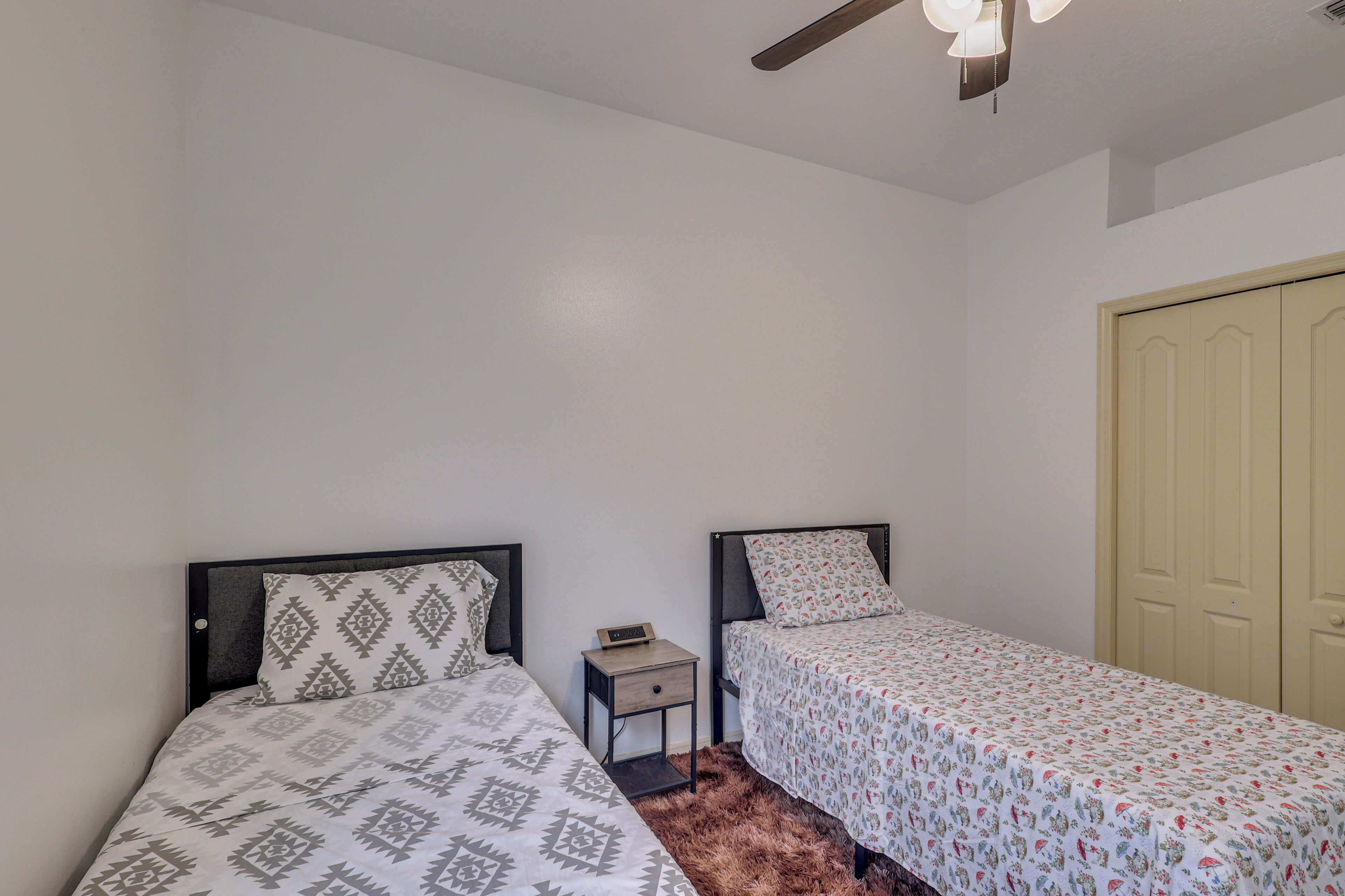A bedroom with two single beds, a nightstand, a wardrobe, and a ceiling fan.