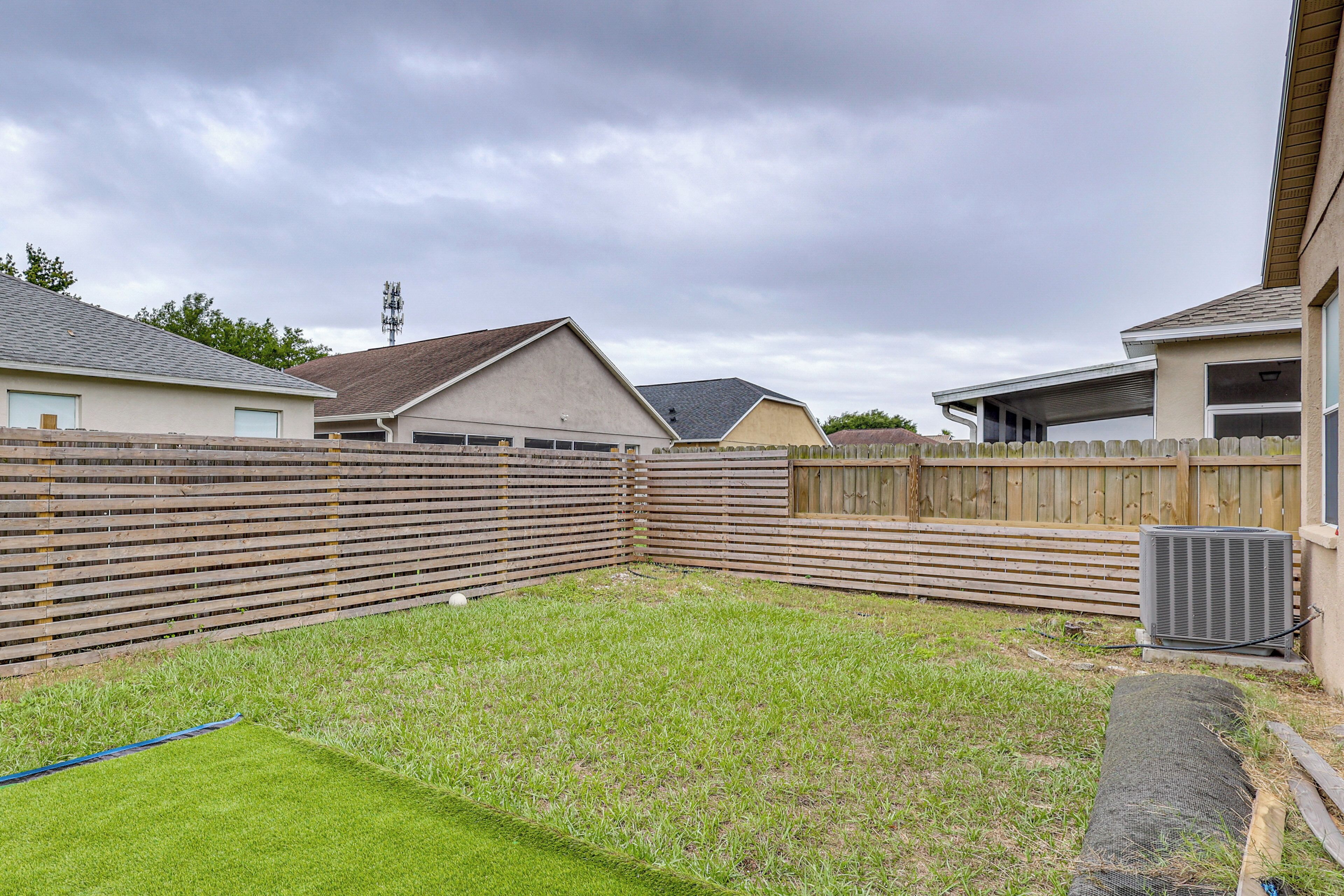 Quintal residencial com cerca de madeira, gramado e casa com garagem.