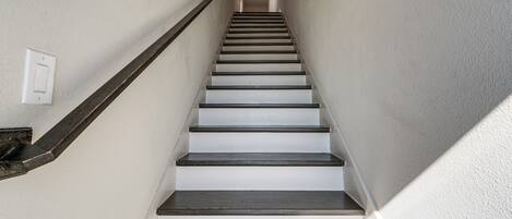 Un escalier avec des marches en bois et une rampe, menant à un palier où se trouve un interrupteur.