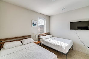 A bedroom with two beds, a window with blinds, a bedside table, a wall-mounted TV, and a ceiling light. - Work & Play! Gem w/ Fire Pit, 3 Mi to Dtwn Dallas (Dallas)