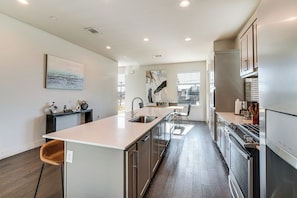 A modern kitchen with a central island, stainless steel appliances, and a large window providing natural light. - Work & Play! Gem w/ Fire Pit, 3 Mi to Dtwn Dallas (Dallas)