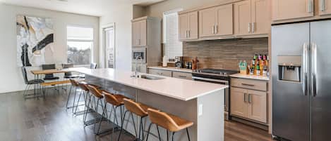 A modern kitchen with a central island, bar stools, stainless steel appliances, and wooden flooring.