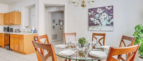 A dining area with a glass table, wooden chairs, and a chandelier.