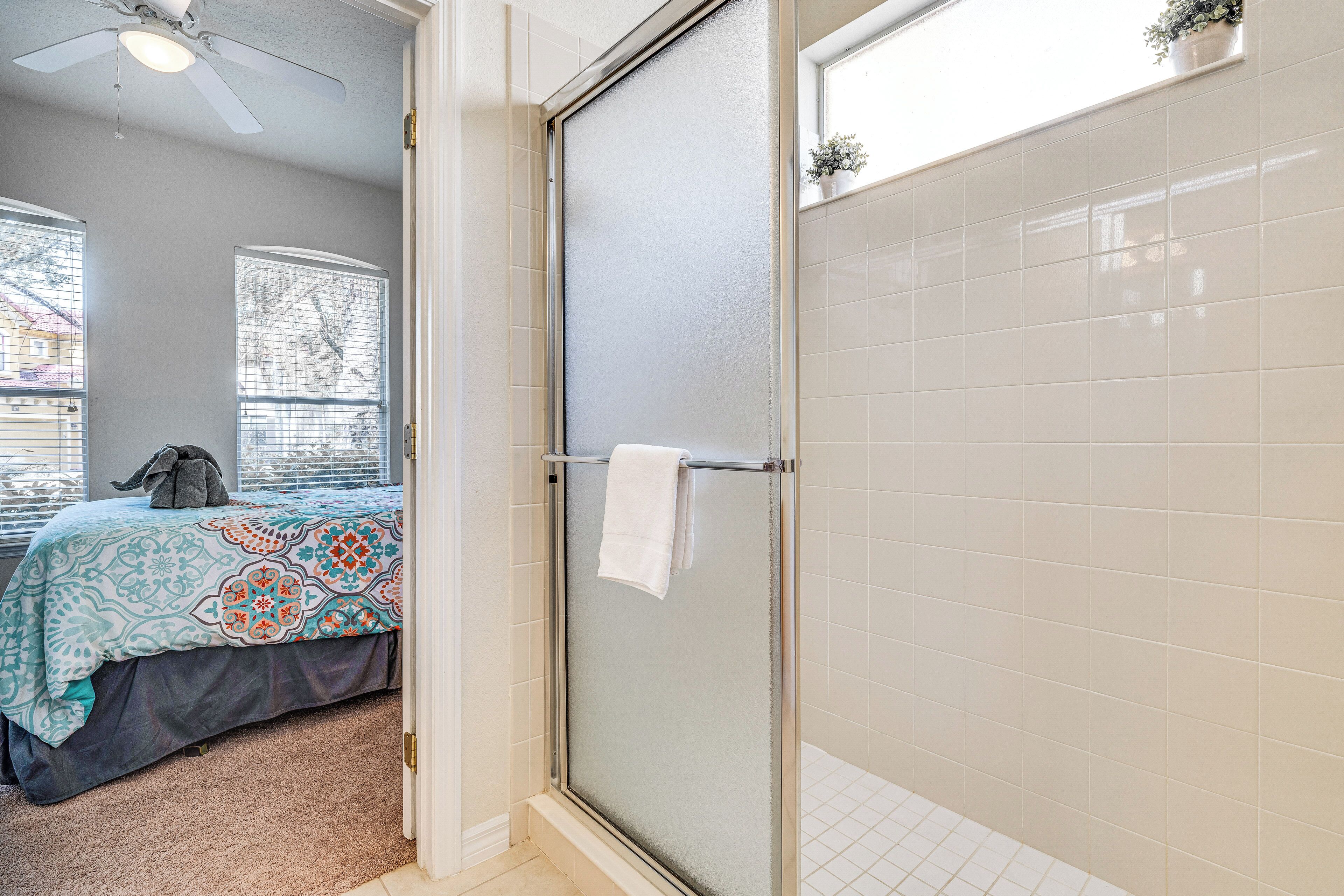 A bathroom with a glass shower door, a towel rack, and a bed with a patterned bedspread.