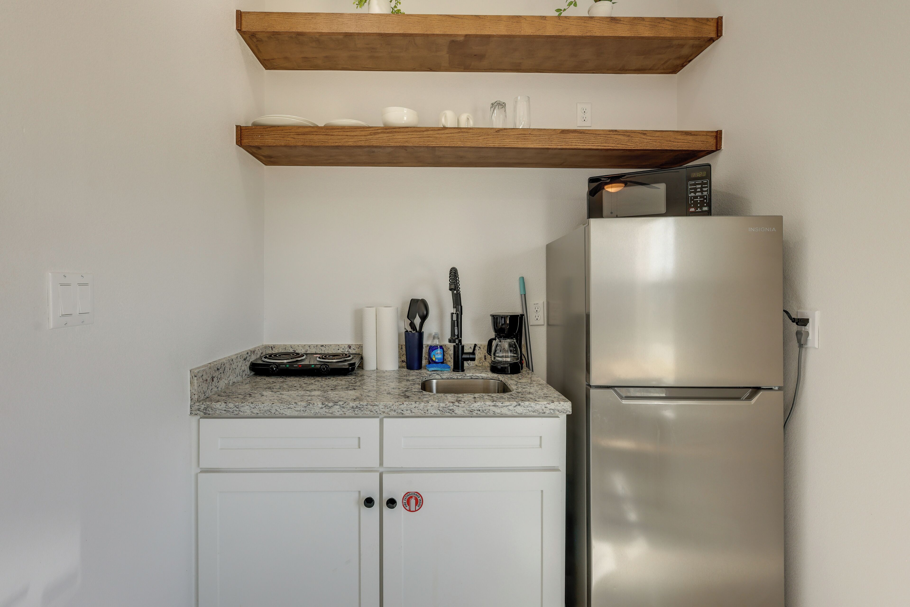 A kitchen with a stainless steel refrigerator, a granite countertop, and wooden shelves above.