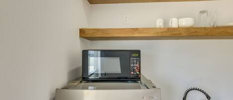 A kitchen with a stainless steel refrigerator, a microwave, a wooden shelf above, and a faucet.