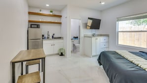 Habitación pequeña con cama, escritorio, kitchenette y televisión.