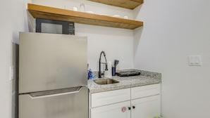 Una cocina compacta con un refrigerador de acero inoxidable, una encimera de granito, un lavamanos y estantes de madera arriba.